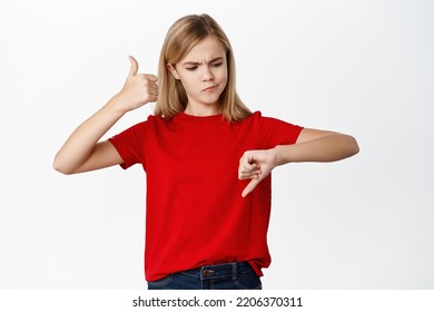 Portrait Of Child, Teen Little Girl Showing Thumbs Up And Thumbs Down, Decision And Weighing Concept, Like Or Dislike, Making Choice, Standing Over White Background.