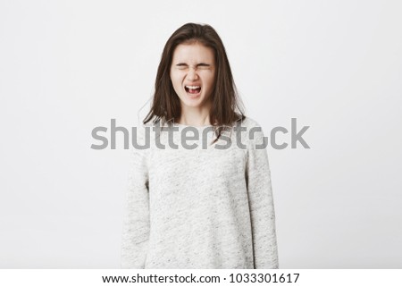 Portrait of childish teenager who is about to cry, standing with closed eyes and screaming out loud. Girl bumped into door with toe and now suffers from huge pain, cursing everything