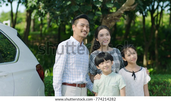 portrait of Chinese parents and kids standing\
outdoors beside car and\
smiling