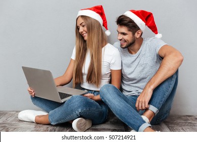 Portrait Of Christmas Couple With Laptop. Sitting Down. Gray Background