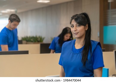 A Portrait Of A Cleaning Lady In The Office Space.Cleaners In The Backgraund.All Of Them Wear Blue Uniforms