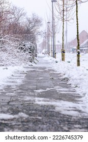 A portrait of a cleared sidewalk from snow made of stone tiles. The walk way is still covered with some frost and ice. If not cleared, the pavement is dangerous and slippery for pedestrians. - Shutterstock ID 2226745379