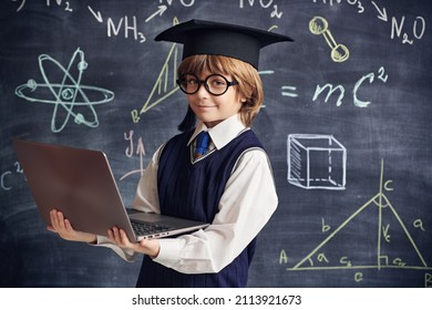 Portrait of a clever little boy in school uniform and glasses holding a laptop in the background of a blackboard with scientific formulas and diagrams. Smart children. Education.  - Shutterstock ID 2113921673