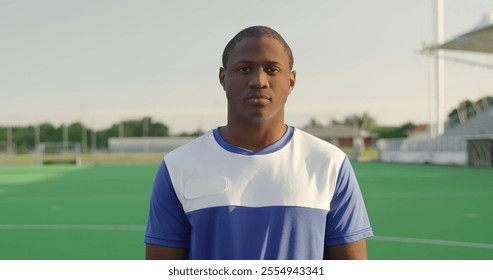 Portrait close up of an African American male field hockey player, wearing a blue team strip, standing on a hockey pitch looking to camera, - Powered by Shutterstock