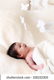 Portrait Of A Close Up Baby Lying On The Bed With Toy Mobile. One Month Old