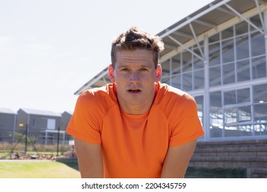 Portrait Close Up Of A Caucasian Male Runner Training At A Sports Field, Wearing An Orange T Shirt, Leaning Forward And Resting, Looking Straight To Camera