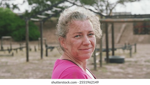 Portrait close up of an exhausted Caucasian woman wearing a pink t shirt standing at boot camp, resting after training, looking to camera and smiling, in slow motion - Powered by Shutterstock