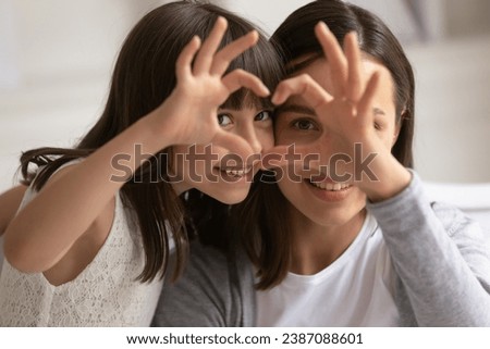 Portrait close up happy mother and daughter showing heart sign with fingers, looking at camera, smiling young mum and adorable cute little girl having fun, child and mom connection and unity