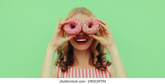 Portrait close up of happy smiling young woman with two donuts having fun on a green background