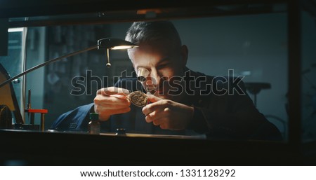 Portrait close up of a professional watchmaker repairer working on an old vintage pocket watch in a workshop. 