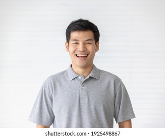 Portrait Close Up Shot Of Handsome Asian Male Model With Short Black Hair Wearing Gray Polo Shirt Stand Smiling In Front Of White Background.