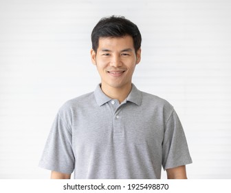 Portrait close up shot of handsome asian male model with short black hair wearing gray polo shirt stand smiling in front of white background.