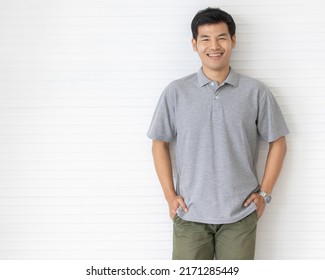 Portrait Close Up Shot Of Handsome Asian Male Model With Short Black Hair Wearing Gray Polo Shirt Stand Smiling In Front Of White Background.