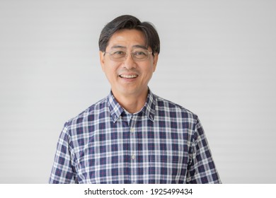 Portrait close up shot of middle aged asian male model with short black hair wearing blue plaid shirt with stand smiling in front of white background.