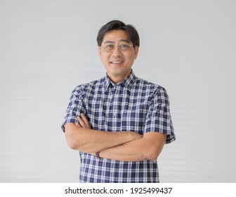 Portrait Close Up Shot Of Middle Aged Asian Male Model With Short Black Hair Wearing Blue Plaid Shirt With Stand Smiling Fold His Arms In Smart Pose On White Background.