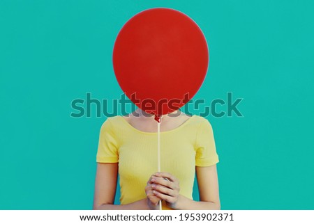 Portrait close up of woman covering her head with red balloon on a blue background