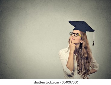 Portrait closeup beautiful thoughtful graduate graduated student girl young woman in cap gown looking up thinking isolated gray wall background. Graduation ceremony future career concept