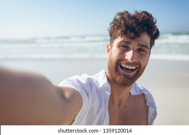 Portrait close-up of happy handsome young Caucasian man taking a selfie standing and at beach on sunny day. He is smiling and looking at camera - Powered by Shutterstock