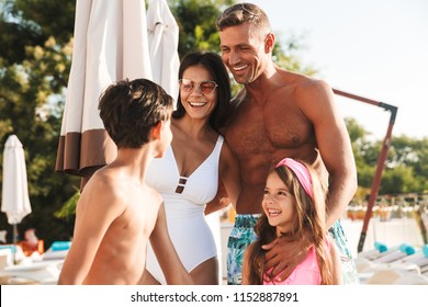 Portrait Closeup Of Joyful European Man And Woman With Kids Smiling While Resting Near Luxury Swimming Pool With Deckchairs And Umbrellas During Vacation