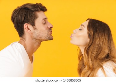 Portrait Closeup In Profile Of Caucasian Couple Man And Woman Kissing Each Other With Eyes Closed While Standing Face To Face Isolated Over Yellow Background