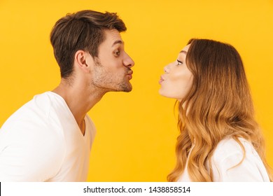 Portrait Closeup In Profile Of Lovely Couple Man And Woman Kissing Each Other While Standing Face To Face Isolated Over Yellow Background