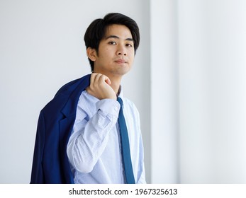 Portrait Closeup Shot Of Asian Young Handsome University Teen Law Student Take Blue Formal Jacket Uniform Off Hold It On Shoulder Standing Look At Camera In Front Of White Wall Background Alone.