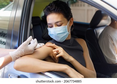 Portrait Closeup Shot Of Female Patient Sit In Drive Thru Queue Look At Camera Point And Receive Coronavirus Vaccine Injection Shot On Shoulder From Syringe On Doctor Hand Wears Rubber Gloves.