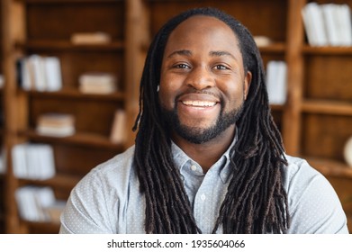 Portrait close-up of a smiling young handsome African American man with dreadlocks standing posing in the library or and looking at the camera, the optimistic black man office manager is ready to work