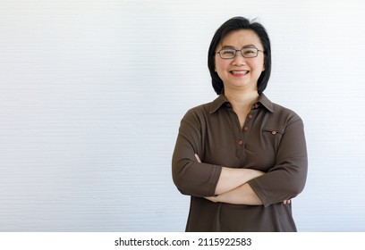 Portrait closeup studio shot of Asian happy middle aged short hair female businesswoman model in casual outfit and eyeglasses standing crossed arms smiling look at camera on white wall background. - Shutterstock ID 2115922583