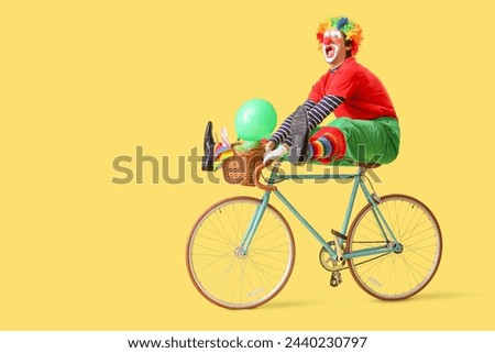 Portrait of clown riding bicycle on yellow background. April Fool's day celebration