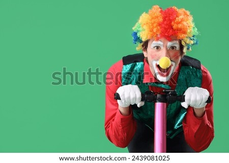 Portrait of clown riding kick scooter on green background. April Fool's day celebration