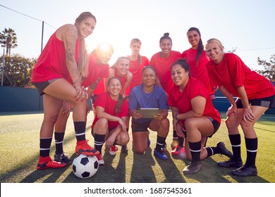 Portrait Of Coach Holding Digital Tablet With Womens Football Team Training For Soccer Match