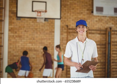 Portrait Of Coach Smiling At Camera While High School Team Playing Basketball In Background