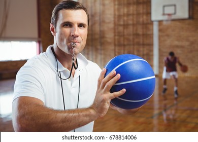 Portrait of coach whistling while holding basketball in court - Powered by Shutterstock