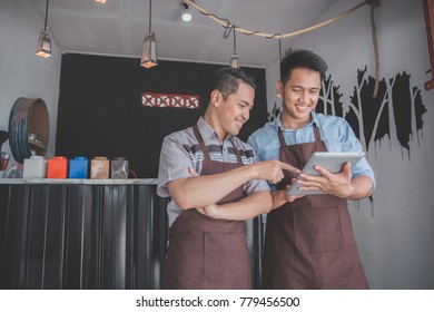 Portrait Of Coffee Shop Owner Discussing With His Employee Using Tablet In Cafe