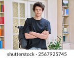 Portrait of college student guy with crossed arms inside educational building