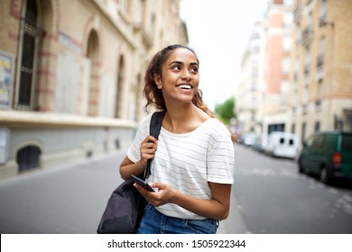 Portrait Of College Student Sitting Outside With Mobile Phone And Looking Away