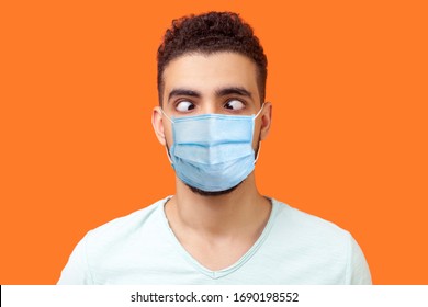 Portrait of comic crazy positive brunette man with surgical medical mask looking cross-eyed, having fun with silly face expression, playing fool. indoor studio shot isolated on orange background