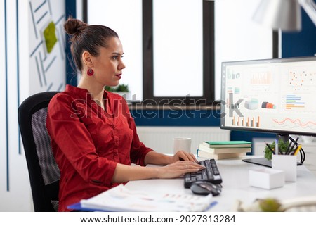Portrait of concentrated entrepeneur working and analyzing financial charts, on computer monitors sitting on desk typing. Start up executive doing research looking at graphs.