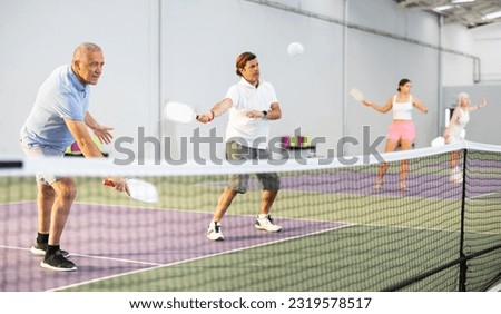 Portrait of concentrated experienced aged pickleball player preparing to strike and return ball to opponents field during doubles match in team with male partner 