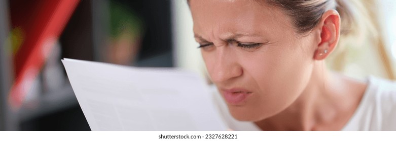 Portrait of concentrated female read papers, squinting to see more clearly. Woman having difficulties seeing text, vision problems