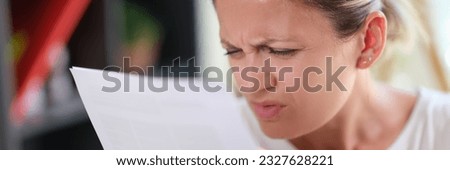 Portrait of concentrated female read papers, squinting to see more clearly. Woman having difficulties seeing text, vision problems