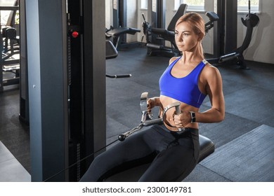 Portrait of concentrated hard working muscular woman performs traction exercise on the waist and pumps back muscles in the gym, wearing sports top and tights. Indoor shot with window on background. - Shutterstock ID 2300149781