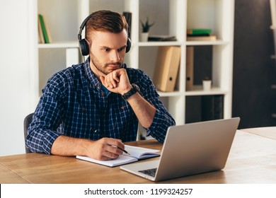 portrait of concentrated man in headphones taking part in webinar at tabletop with notebook in office - Shutterstock ID 1199324257