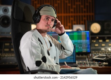 Portrait of concentrated music producer sitting in headphones in sound recording studio. Sound engineer wearing cap and sweatshirt listening to sound track. Creating music concept - Powered by Shutterstock