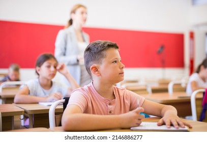 Portrait Of Concentrated Tween Boy Studying In Classroom, Listening To Schoolteacher And Writing In Notebook