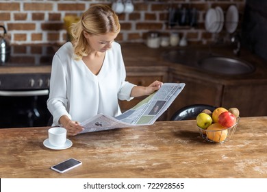 portrait of concentrated woman reading newspaper while sitting at table with smartphone and cup of coffee - Powered by Shutterstock