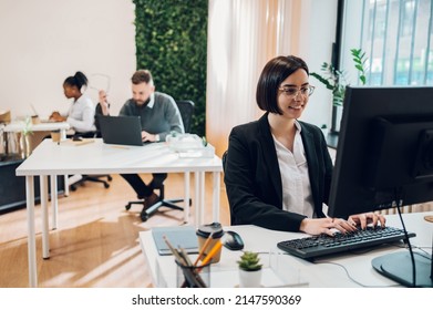 Portrait Of A Concentrated Young Business Woman Working On A Laptop While Sitting At The Table In The Office. Confident Business Expert. E-commerce, Internet Technology Or Small Business Concept.