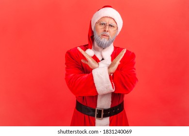 Portrait Of Concerned Serious Man In Eyeglasses And Red Santa Claus Clothes Showing X Gesture With Hands, This Is The End And No Way More. Indoor Studio Shot Isolated On Red Background