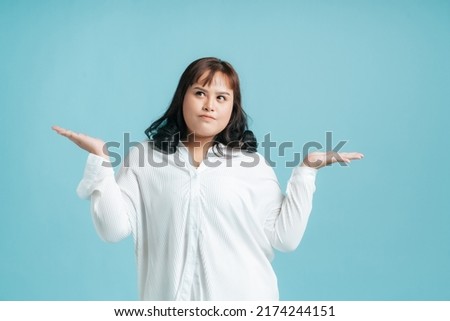 Portrait Confidence beautiful Asian woman plus size posing thinking with choice on hands opening to copy space aside on isolate light blue studio background. Young female chubby confident concept.